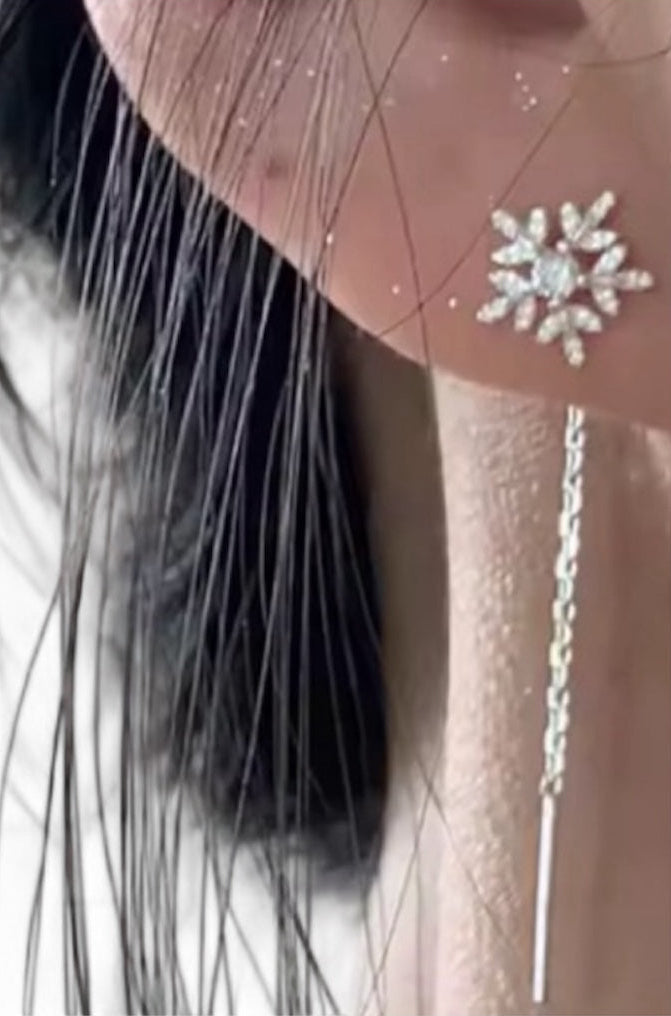 Close-up of a silver snowflake earring with a chain back on an ear against a neutral background.