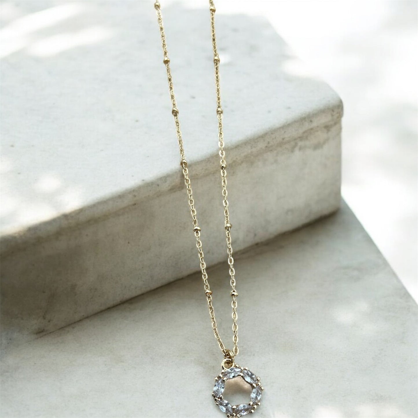 Gold necklace with a circular pendant on a marble surface