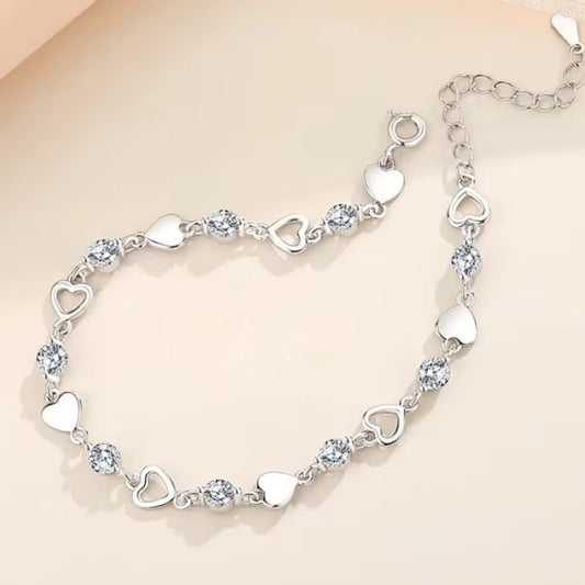 Silver bracelet with heart-shaped links and clear crystals on a beige background