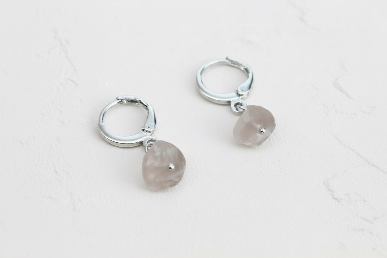Silver hoop earrings with stone pendants on a linen background.