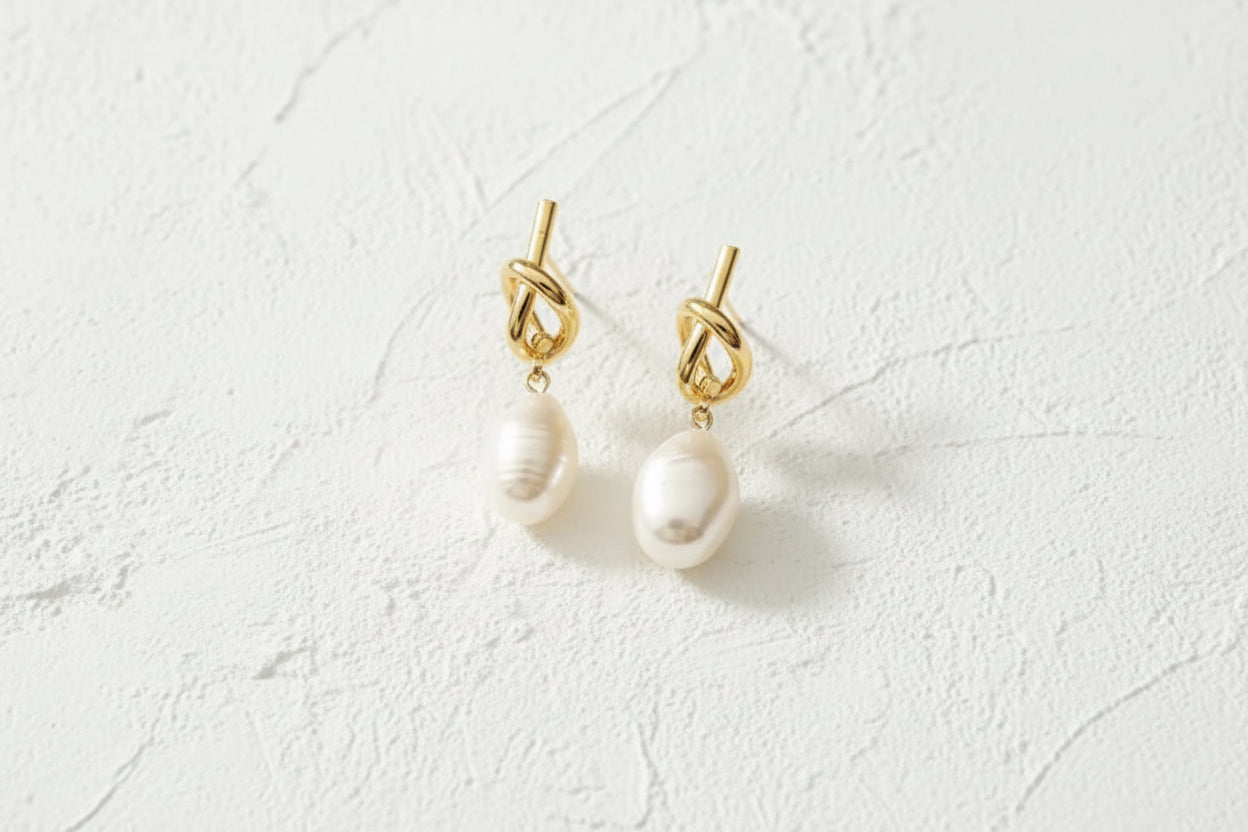 Gold earrings with pearl drops on a beige surface.