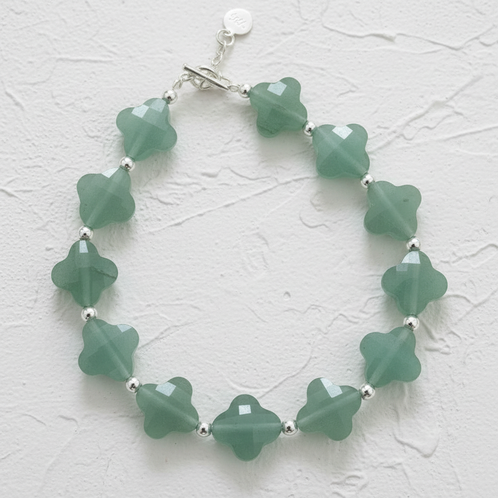 Green beaded bracelet with silver accents on a textured beige background.