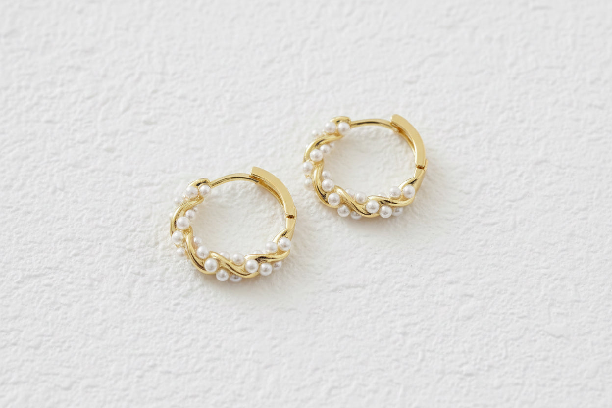 Gold hoop earrings with small pearl twist accents on a brown material background.