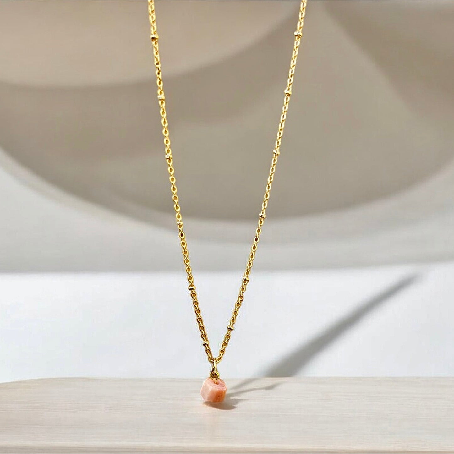 Pink opal raw crystal pendant on a gold chain.