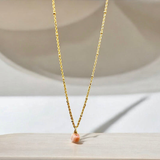Pink opal raw crystal pendant on a gold chain.