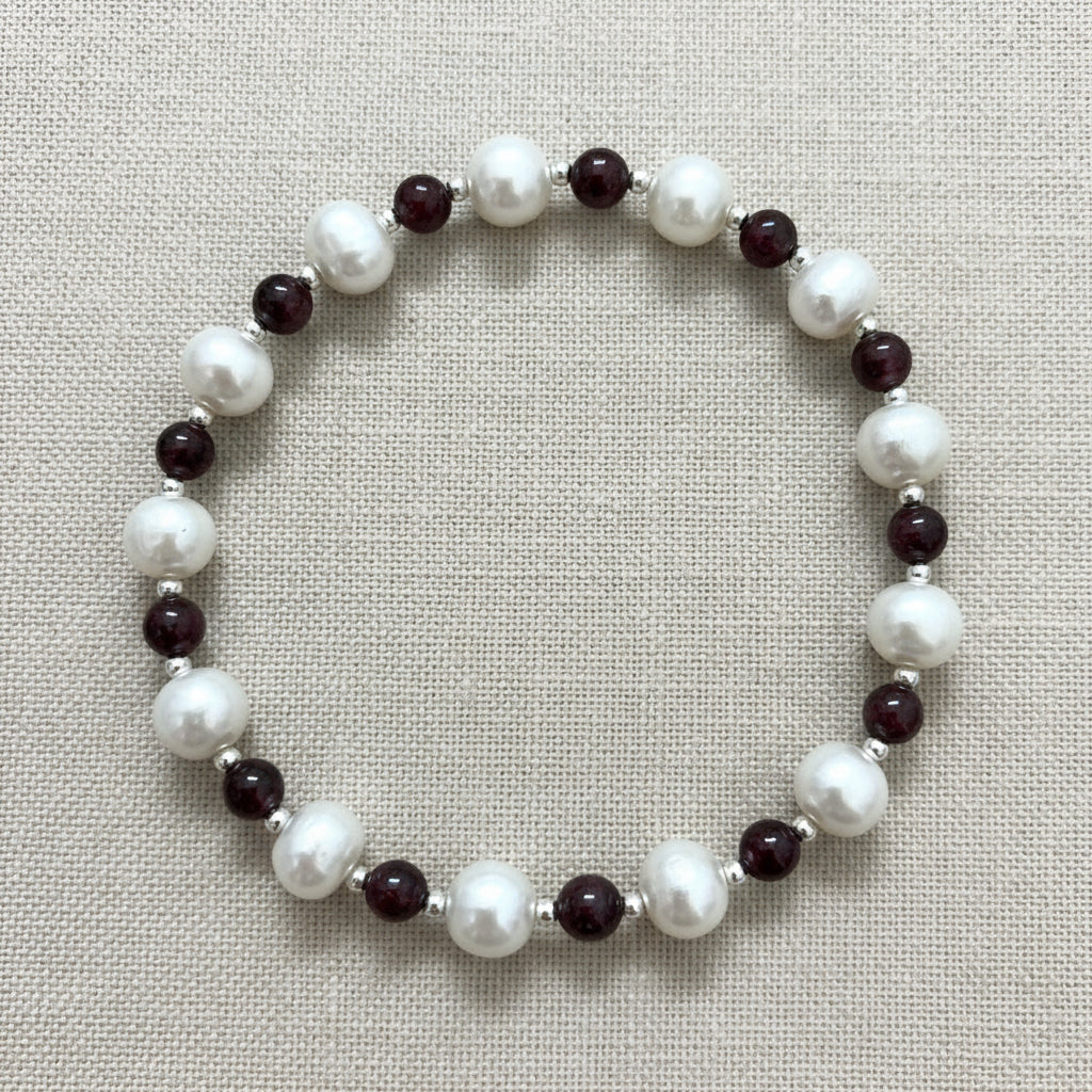 A bracelet with a combination of white fresh water pearls, garnet beads, and silver spacer beads.
