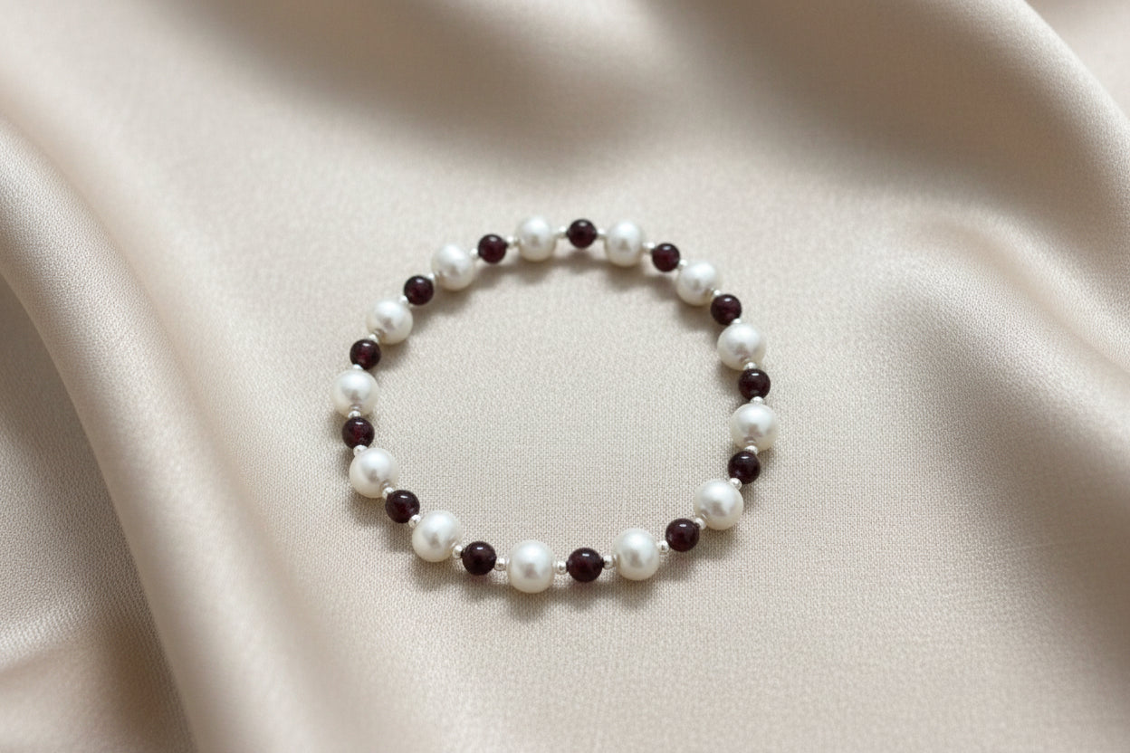 A bracelet with a combination of white fresh water pearls, garnet beads, and silver spacer beads.