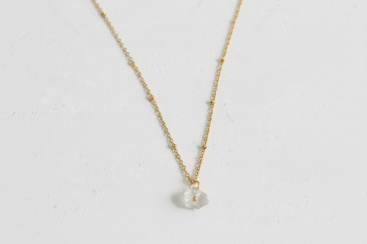 A gold-plated chain necklace with a raw clear quartz crystal pendant.