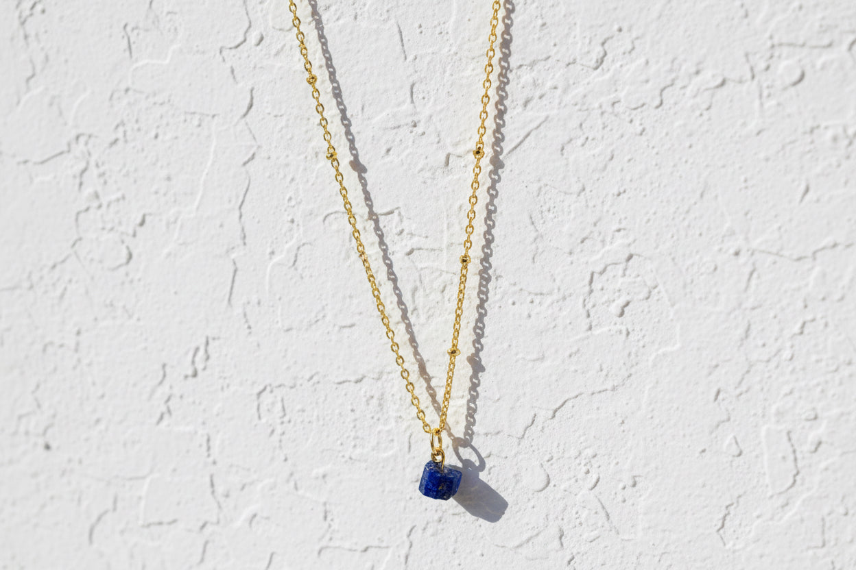 Gold necklace with a blue pendant on a white background.