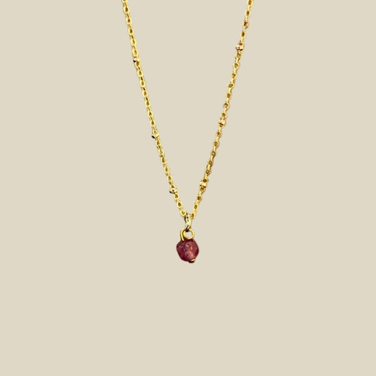 A gold-plated necklace with a single raw ruby crystal pendant.