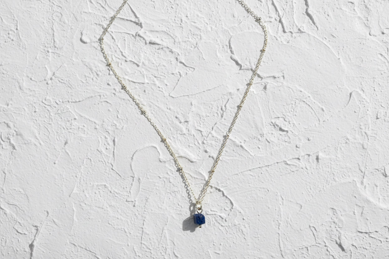 Necklace with a blue pendant on a light beige background.