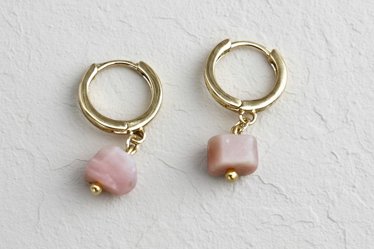 Gold hoop earrings with pink beads on a beige background.
