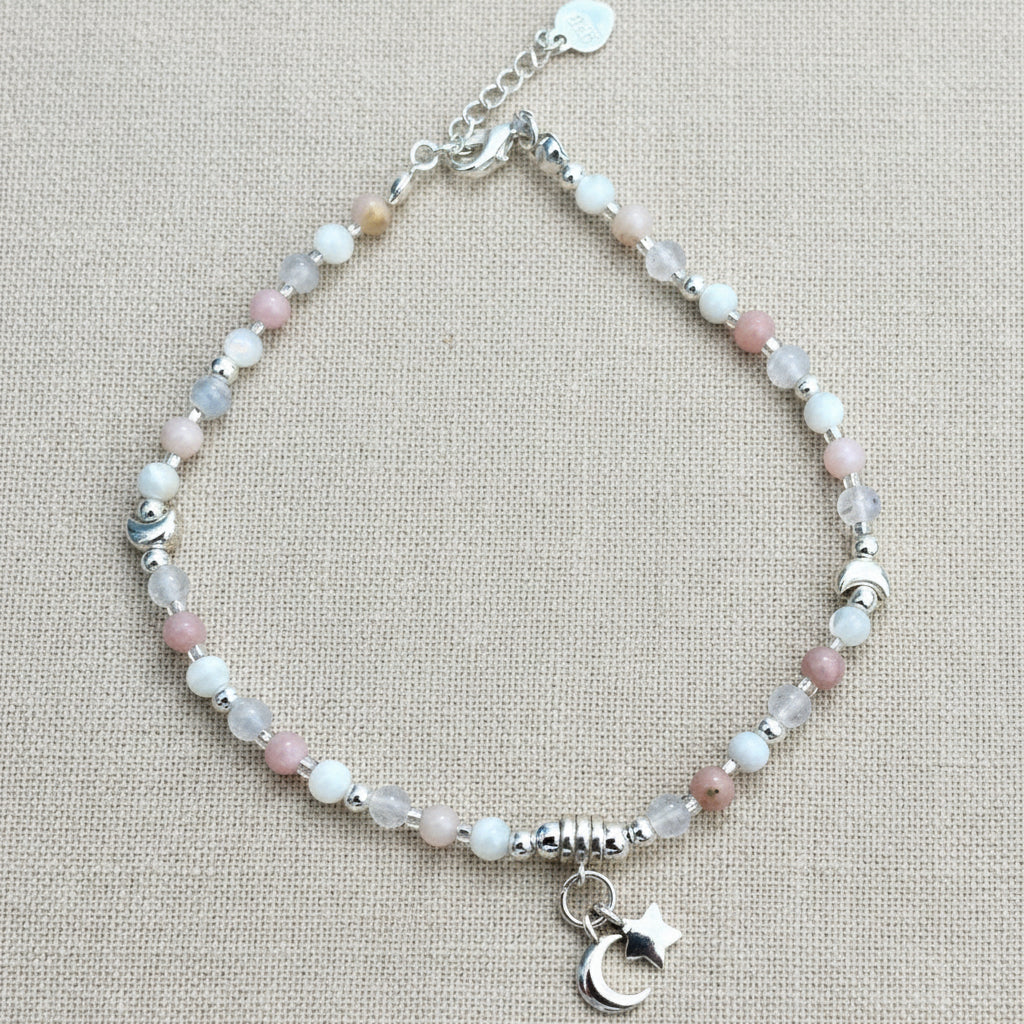 Bracelet with pastel beads and a moon charm on a linen background.