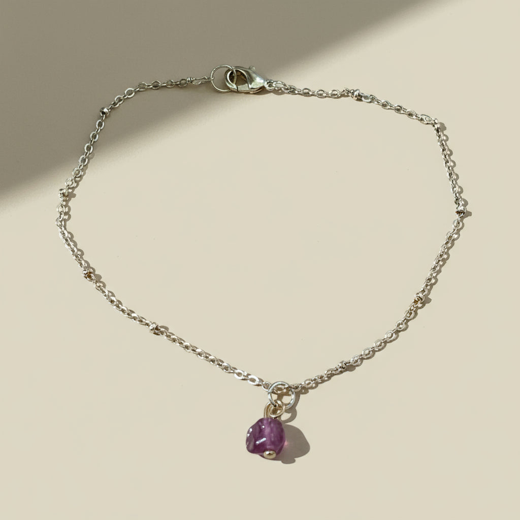 Gold bracelet with a small red gemstone on a beige background.
