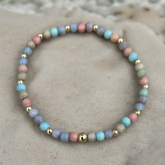 A multicolored agate and gold beaded bracelet on a textured background.
