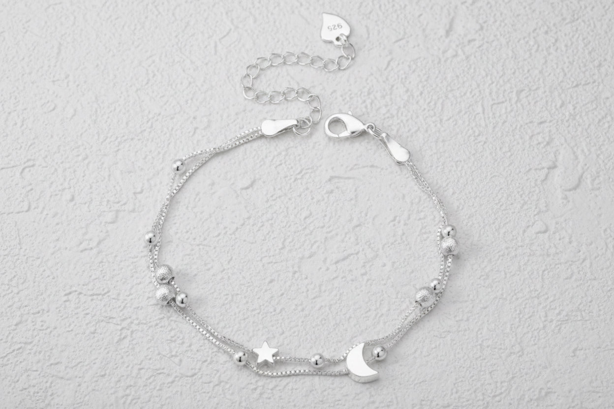 Silver bracelet with star and moon charms on a grey background.