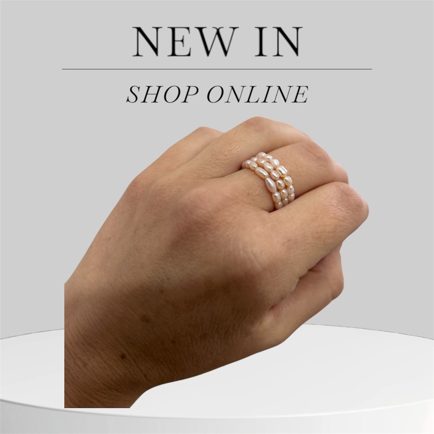 Hand wearing a pearl ring with 'New In' and 'Shop Online' text on a light gray background.