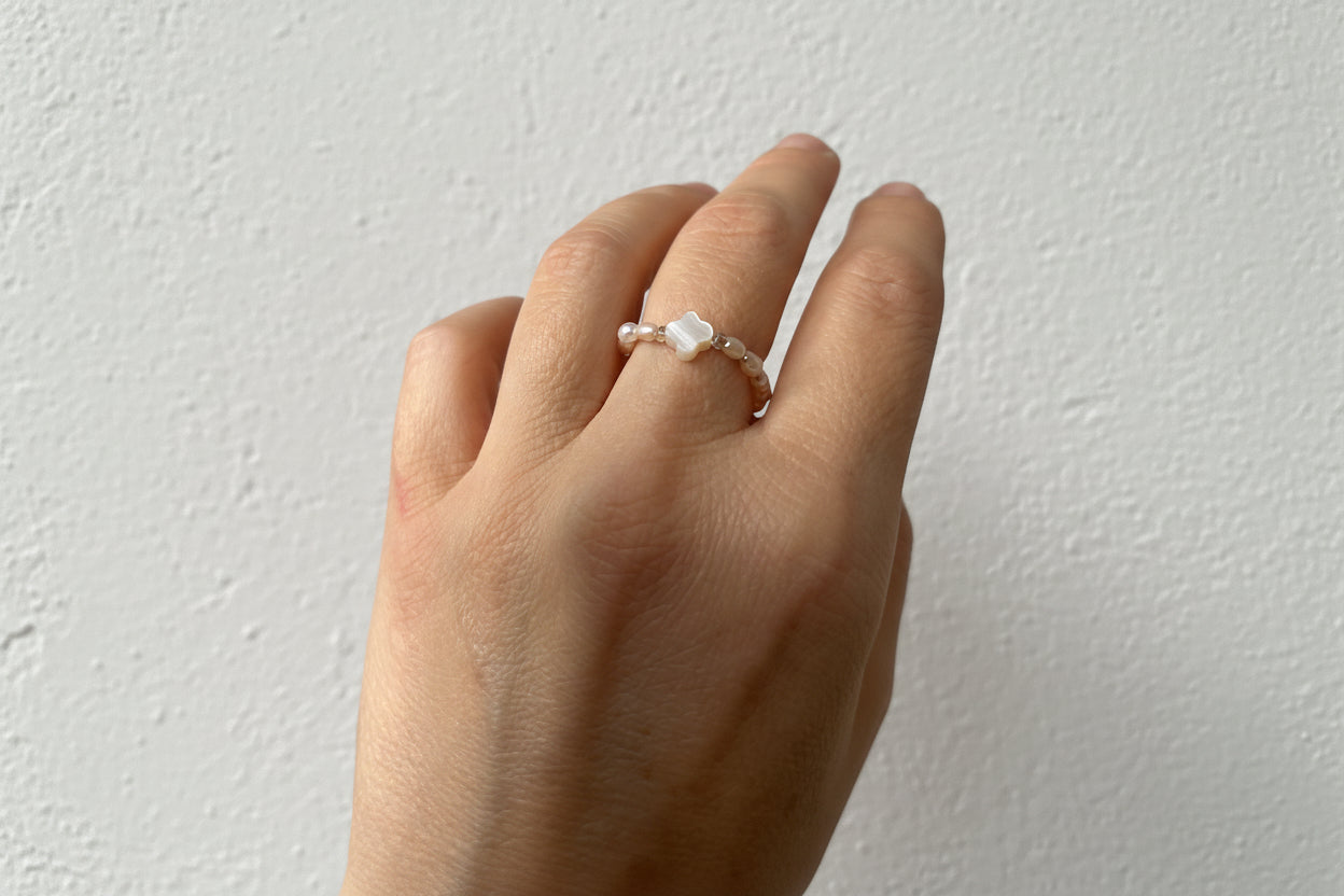 Hand wearing a pearl bead ring with a white clover.
