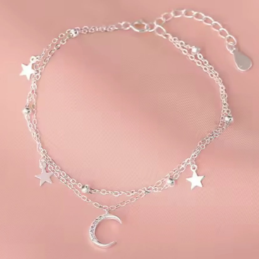 Silver bracelet with star and moon charms on a pink background