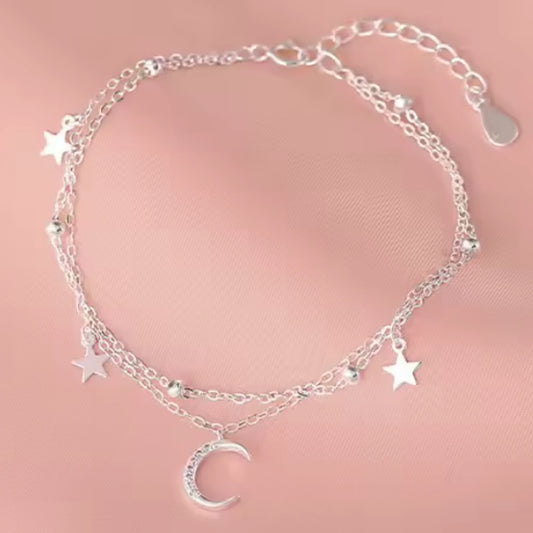 Silver bracelet with star and moon charms on a pink background