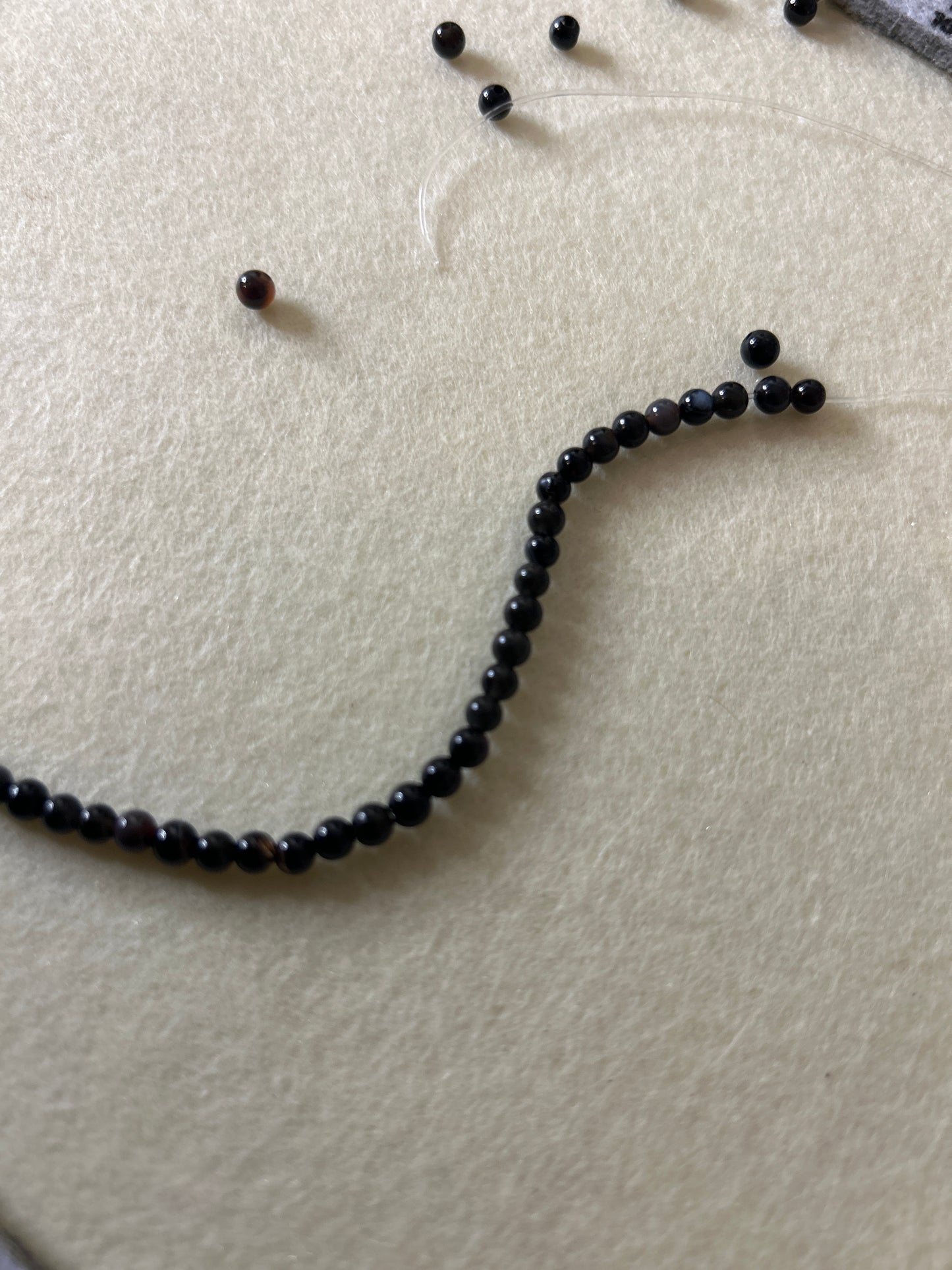 An unfinished black beaded necklace on a textured white surface.