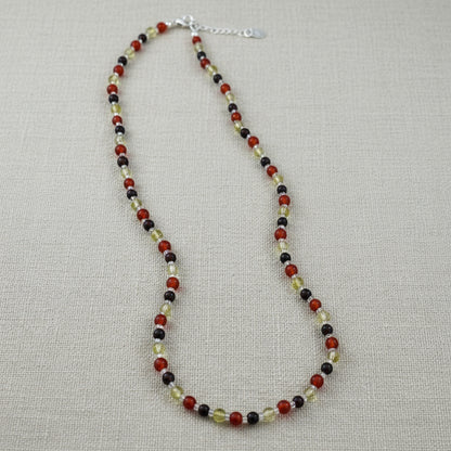 Beaded necklace on a linen surface made with black, red and yellow beads.