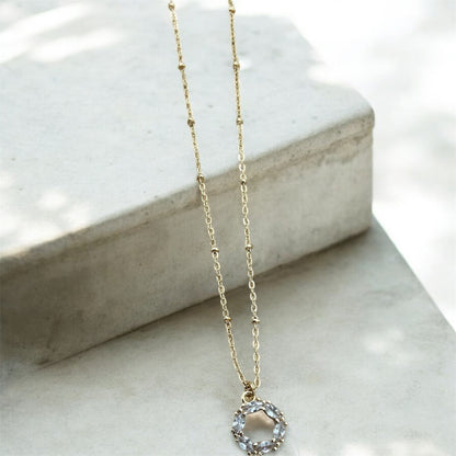 Gold necklace with a circular pendant on a marble surface
