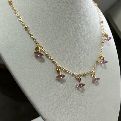 Gold necklace with pink gemstones on a white stand.