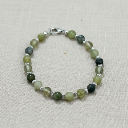 Green beaded bracelet with silver accents on a light fabric background.