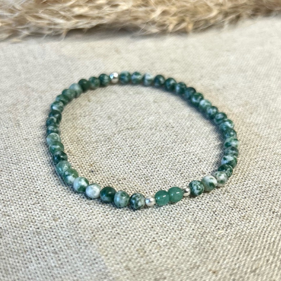 Green beaded bracelet on a textured fabric surface.