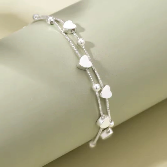 Silver bracelet with heart-shaped beads on a light green background
