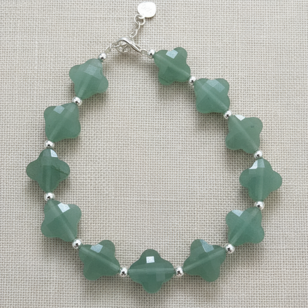 Green beaded bracelet with silver accents on a textured beige background.