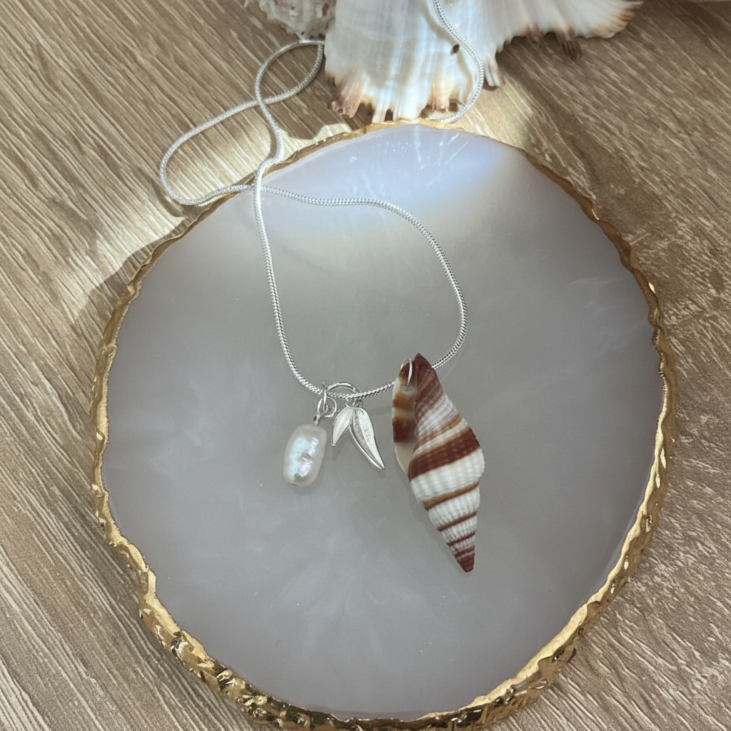 Necklace with a natural shell pendant with a silver leaf charm and pearl on a crystal and wood surface.