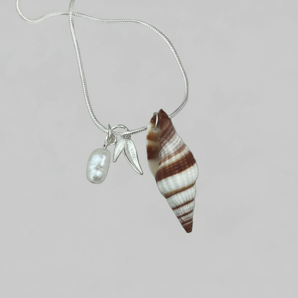 Necklace with shell pendant, silver leaf charm, and pearl on a light background.