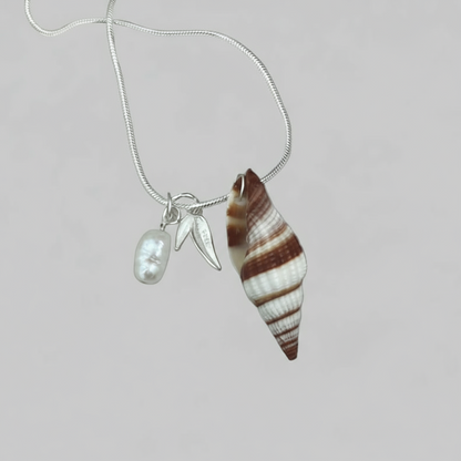 Necklace with shell pendant, silver leaf charm, and pearl on a light background.