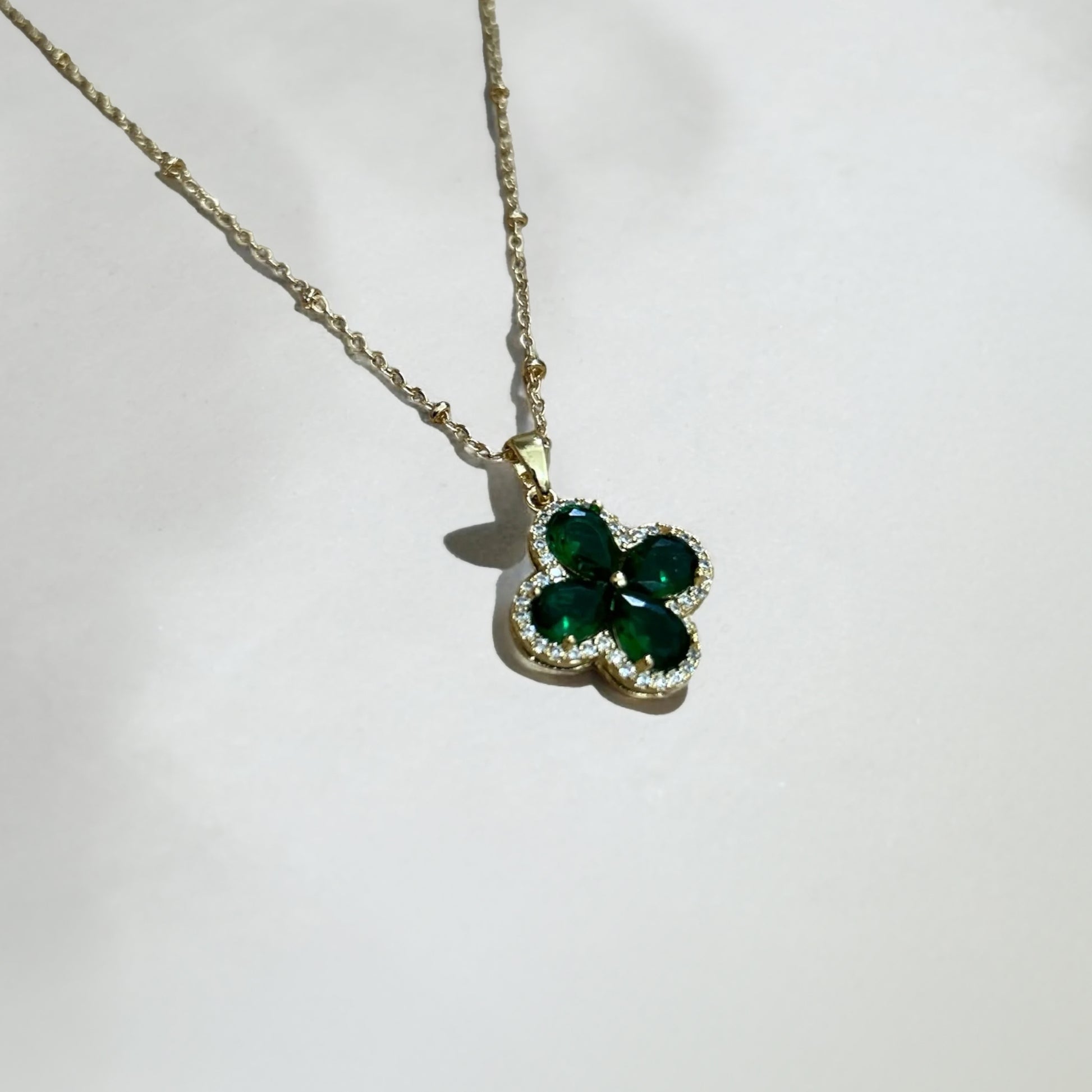 Gold necklace with a green clover-shaped pendant on a white background