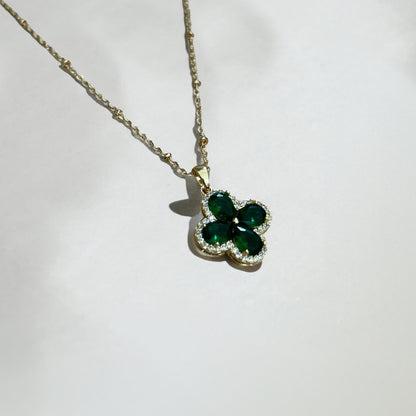 Gold necklace with a green clover-shaped pendant on a white background
