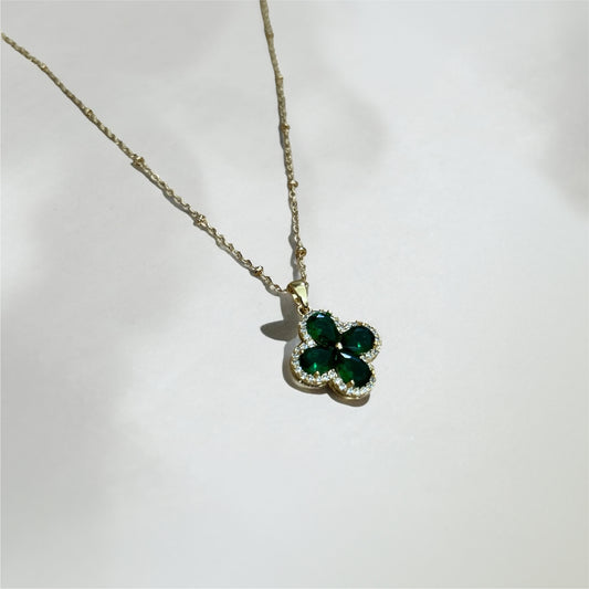 Gold necklace with a green clover-shaped pendant on a white background