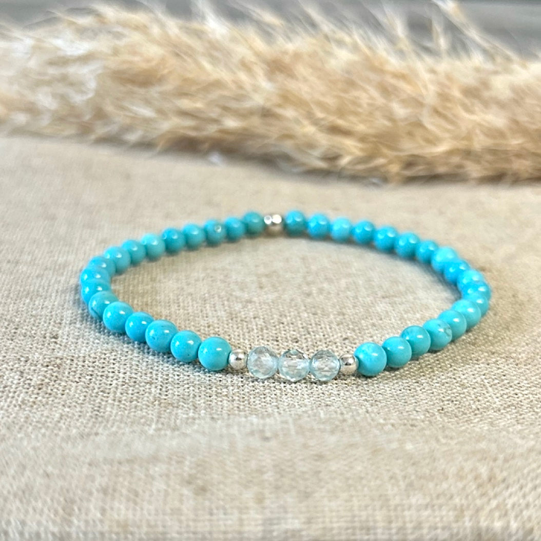 Turquoise beaded bracelet with silver accents on a textured fabric background