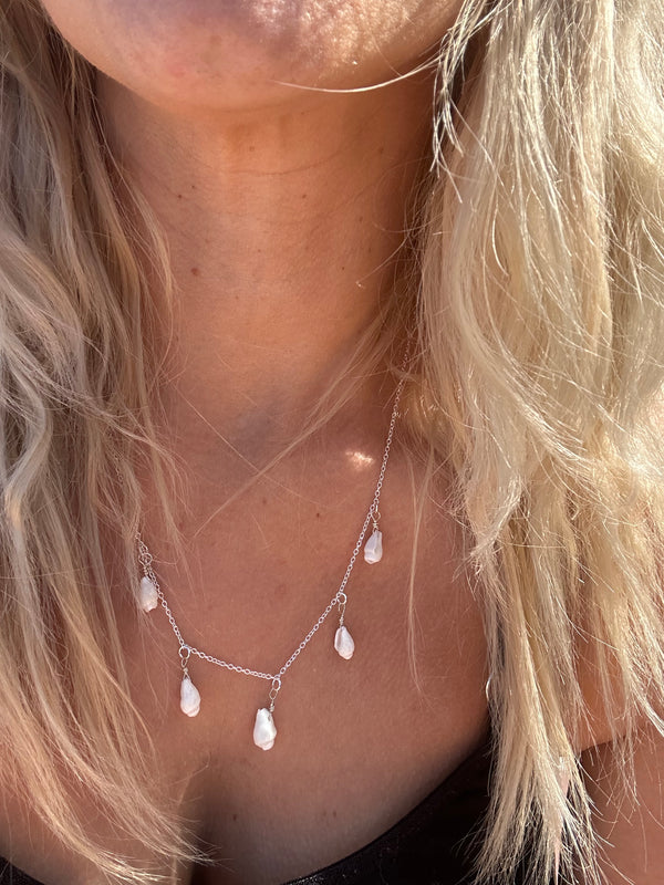 Silver necklace with five small white shells.