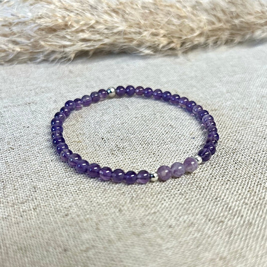 Purple beaded bracelet on a textured surface with dried grass in the background.
