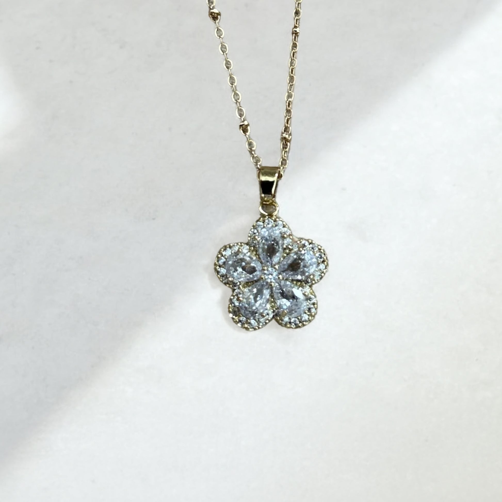 Flower-shaped pendant on a gold chain against a white background