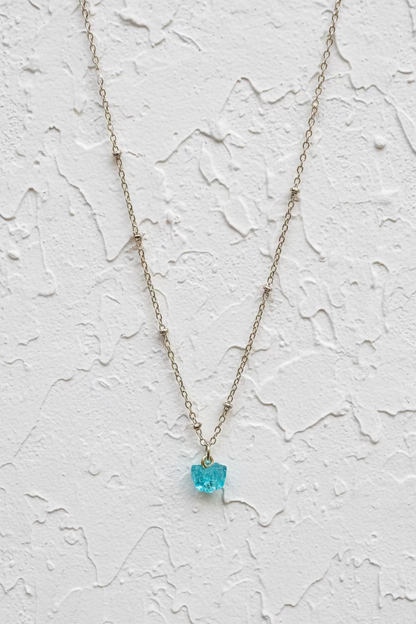 Gold necklace with a blue gemstone on a white background.