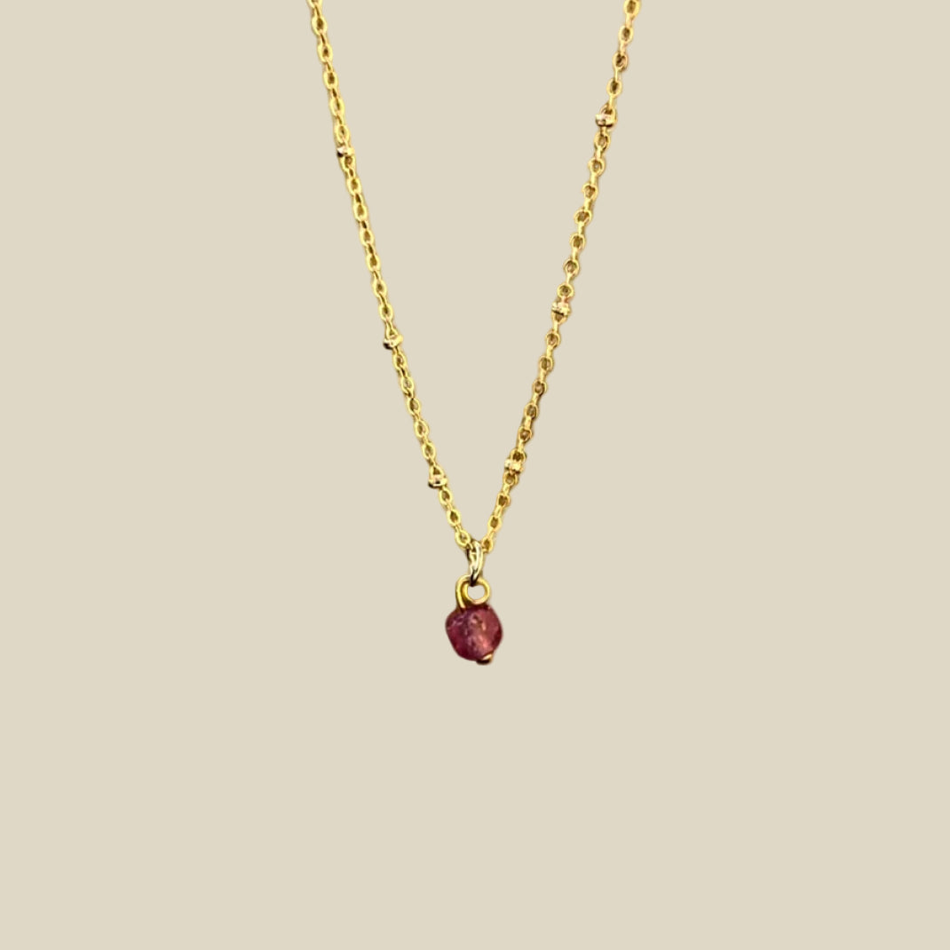 A gold-plated necklace with a single raw ruby crystal pendant.