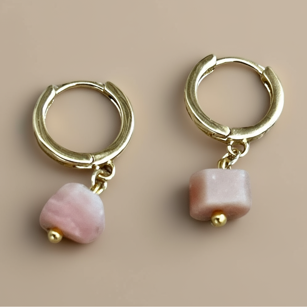 Gold hoop earrings with pink beads on a beige background.