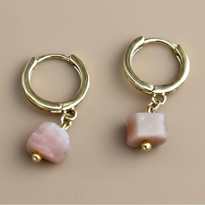 Gold hoop earrings with pink beads on a beige background.