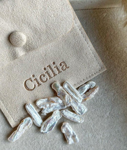 Cicilia branded jewelry pouch with natural biwa pearls on a beige background.