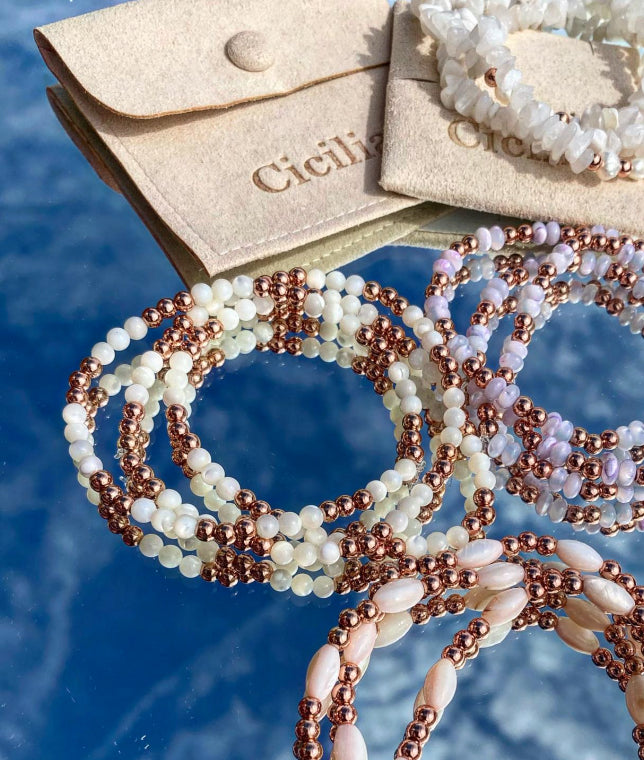 Beaded bracelets with rose gold and white beads on a blue background, featuring Cicilia brand packaging.
