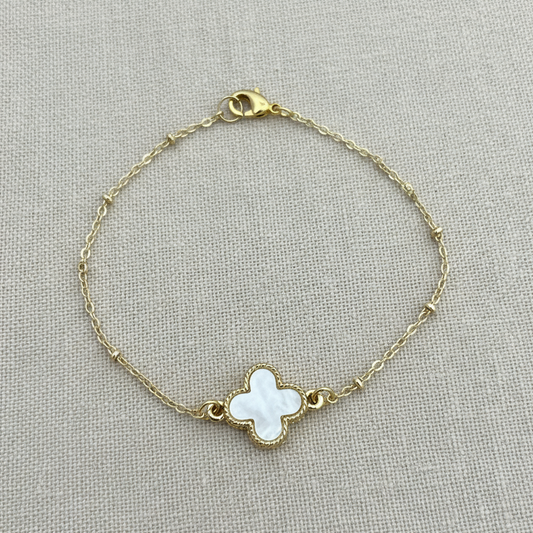 Gold bracelet with a clover-shaped charm on a light gray background