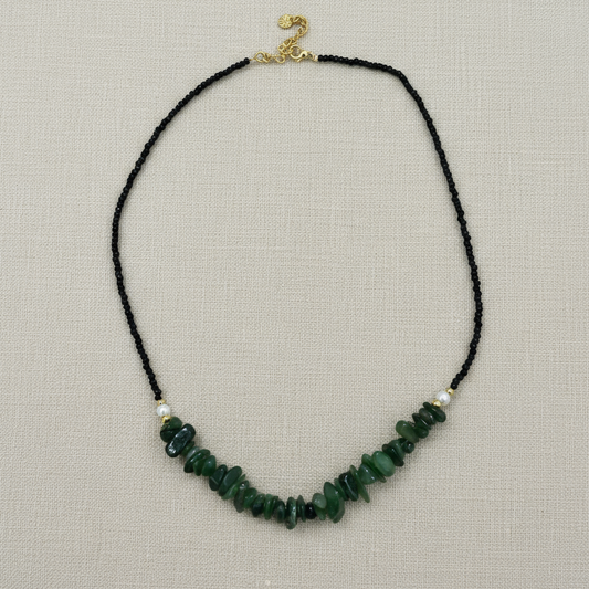 Necklace with green beads on a black cord against a white background